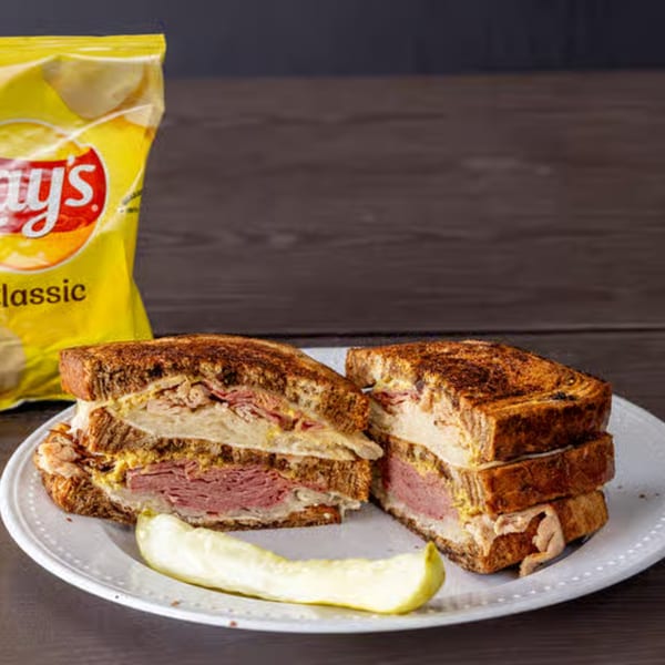 A Weinberger's Deli sandwich, cut in half, with a pickle spear and a bag of chips.