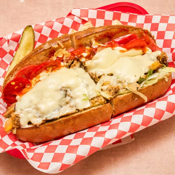 A Weinberger's Deli cheesesteak with melted cheese, red sauce, and a pickle in a red basket.