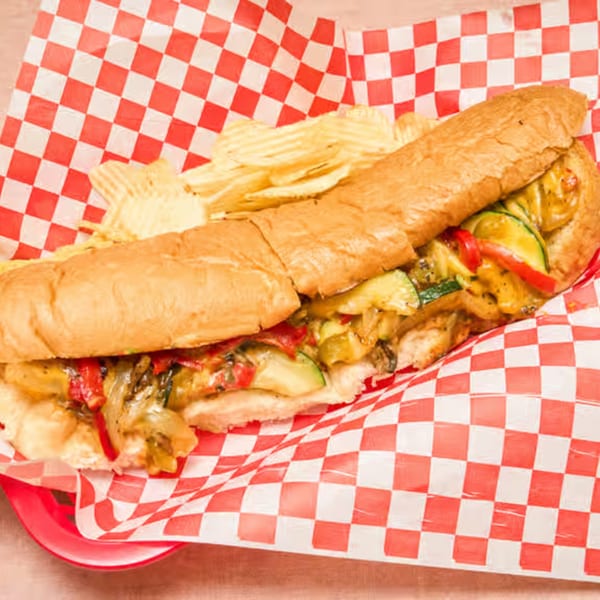 Weinberger's Deli veggie sub sandwich with chips on red and white checkered paper.