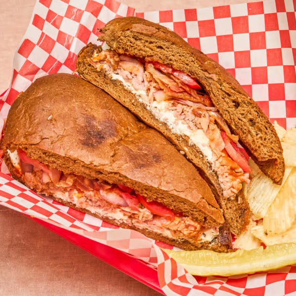 Two deli sandwiches on dark bread with meat, cheese, and tomatoes, served with chips and a pickle.
