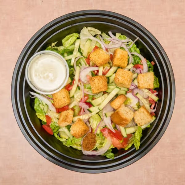 Overhead view of a deli salad with lettuce, tomatoes, cucumbers, red onions, croutons, and dressing.