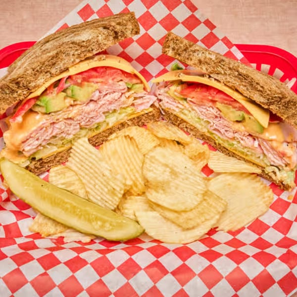 Deli sandwich cut in half, with chips and a pickle, served in a red basket.