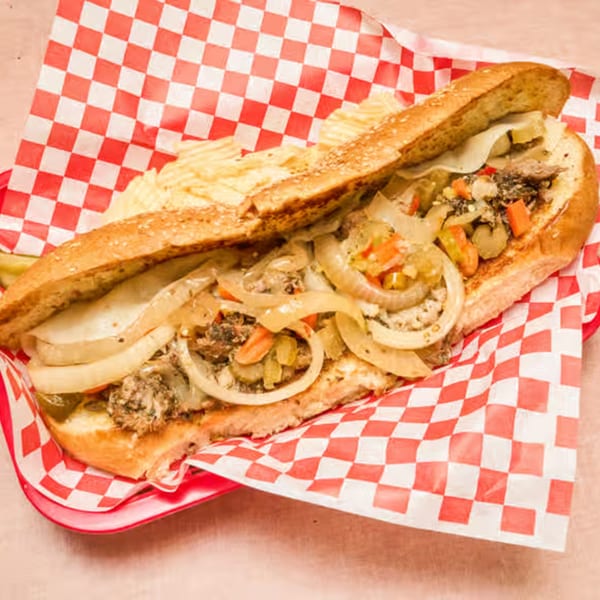 A Weinberger's Deli sandwich with meat, cheese, onions, and vegetables, served with chips.